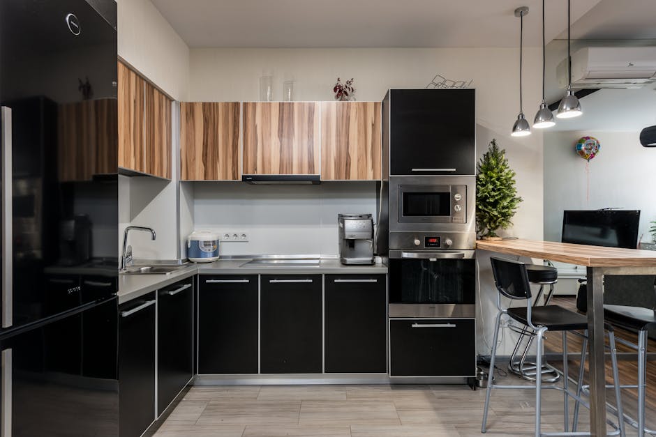 Wooden table with chairs placed near cupboards and counter with sink and appliances in modern kitchen with kitchenware in apartment